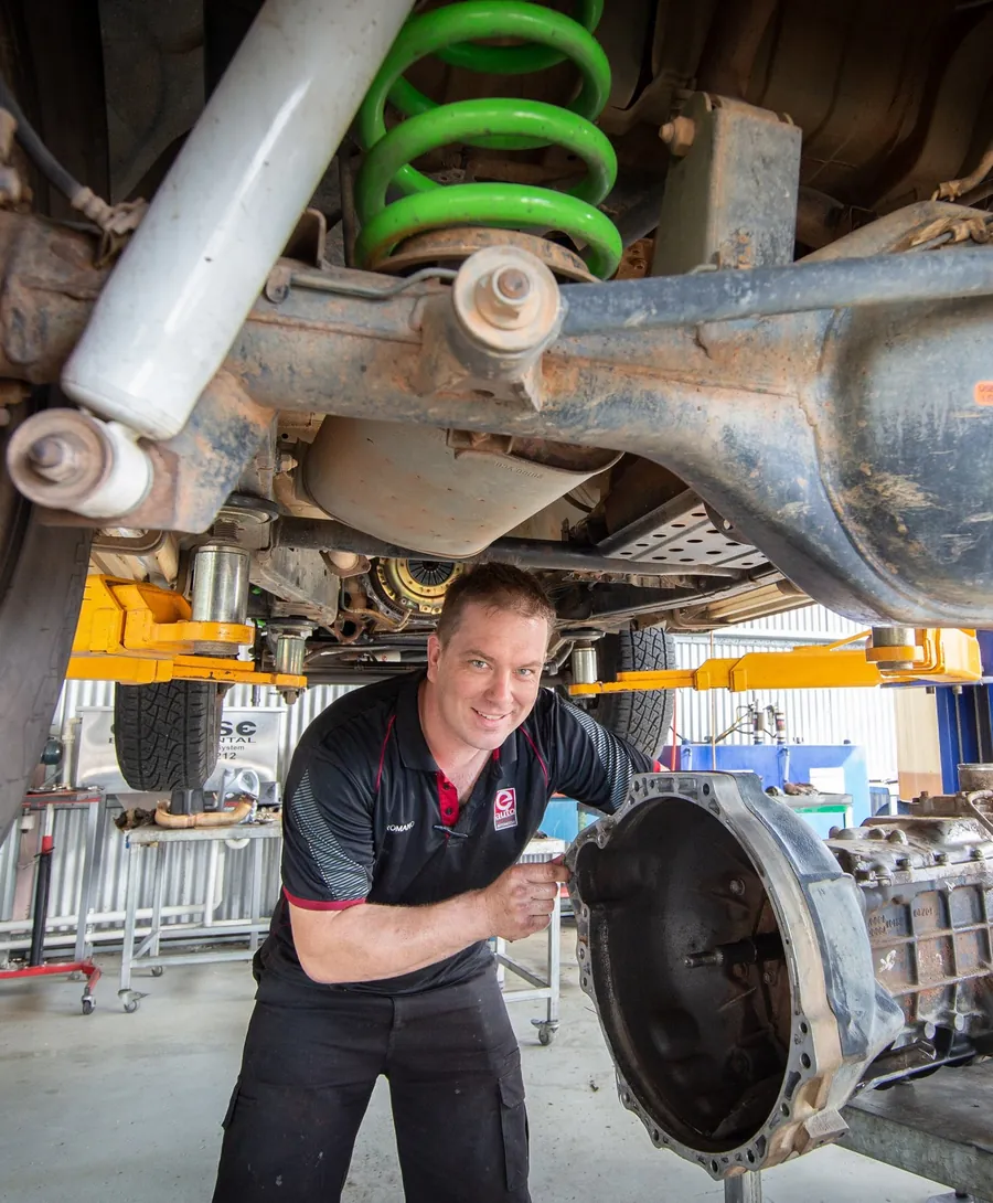 A mechanic lowering a gearbox from under a lifted 4WD